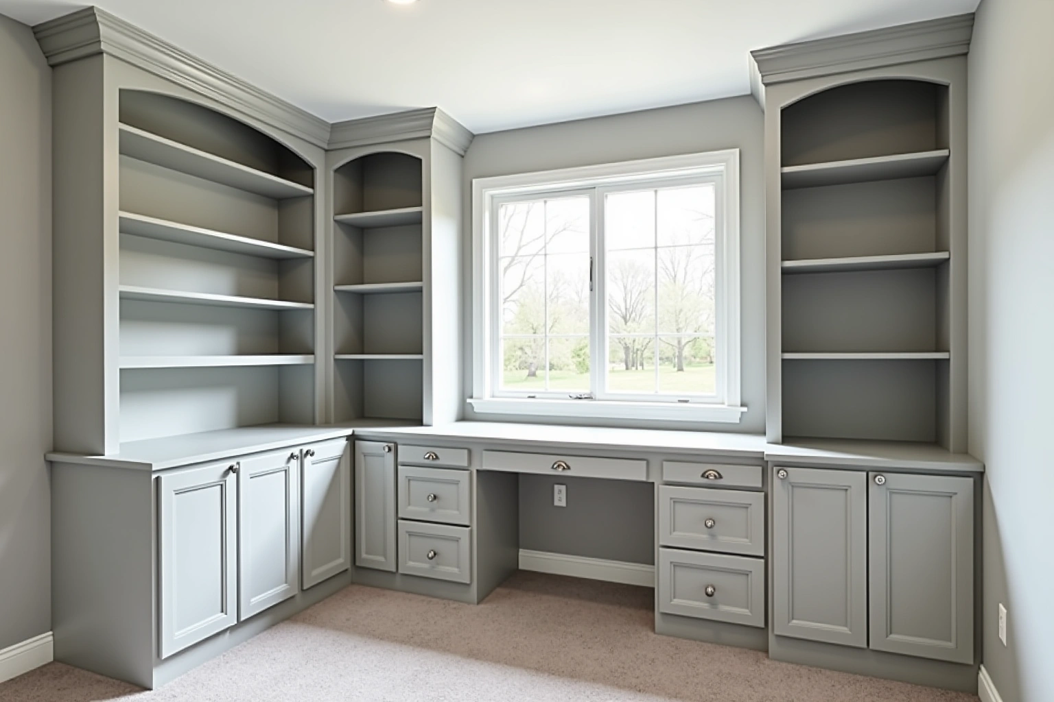 Home office with grey painted built-in bookcases, arched shelf tops, base cabinets and a desk under the window.