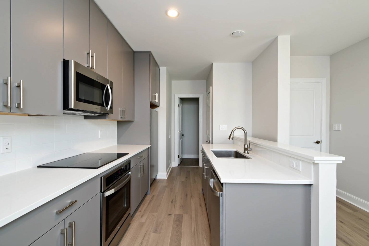 New apartment kitchen with grey flat-panel slab-door cabinets, white quartz counter, a wall oven, induction cooktop, pull-out faucet and wood-look floor.