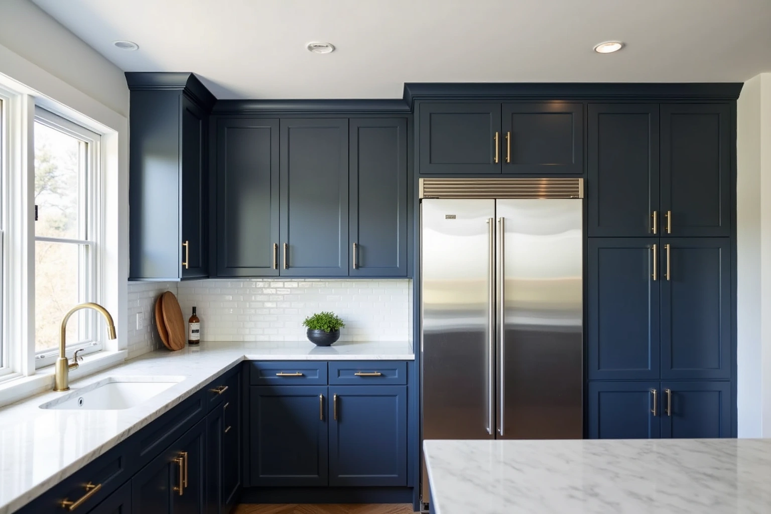 Floor-to-ceiling navy shaker cabinets with brass pulls around a stainless refrigerator, white subway tile and marble counters.