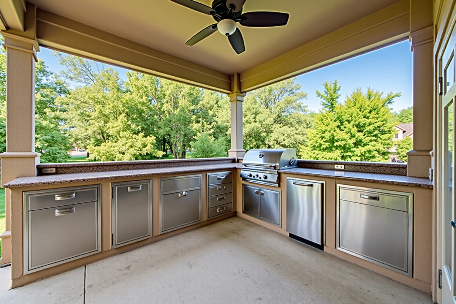 Covered patio kitchen with stainless steel drawers and doors set in a stucco base under granite counters and a grill.